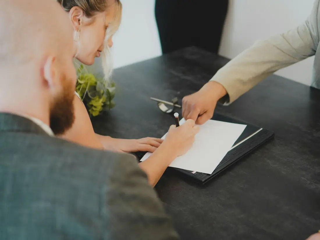 People reviewing and signing a document at a dark table