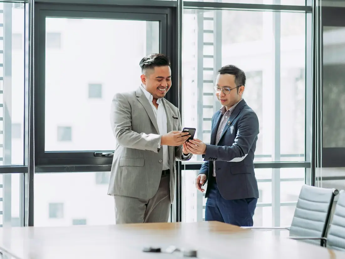Two men in a conference room looking at a phone