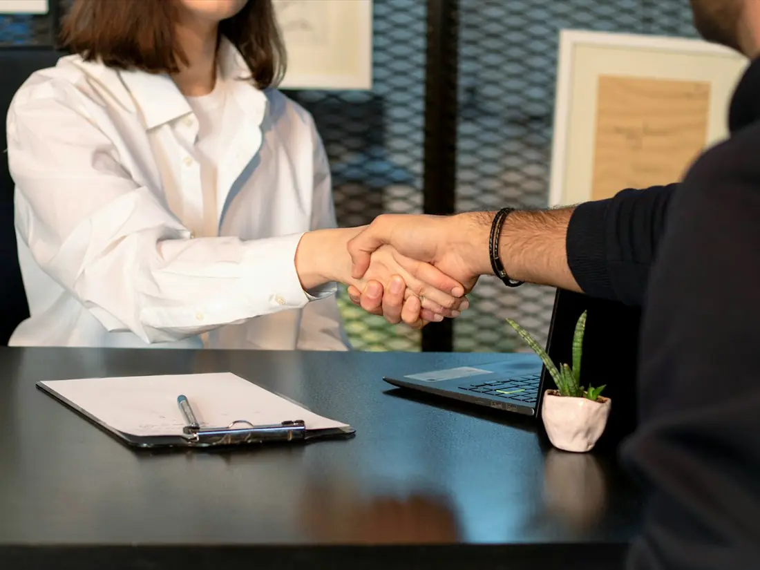 A handshake across a desk with a clipboard in front